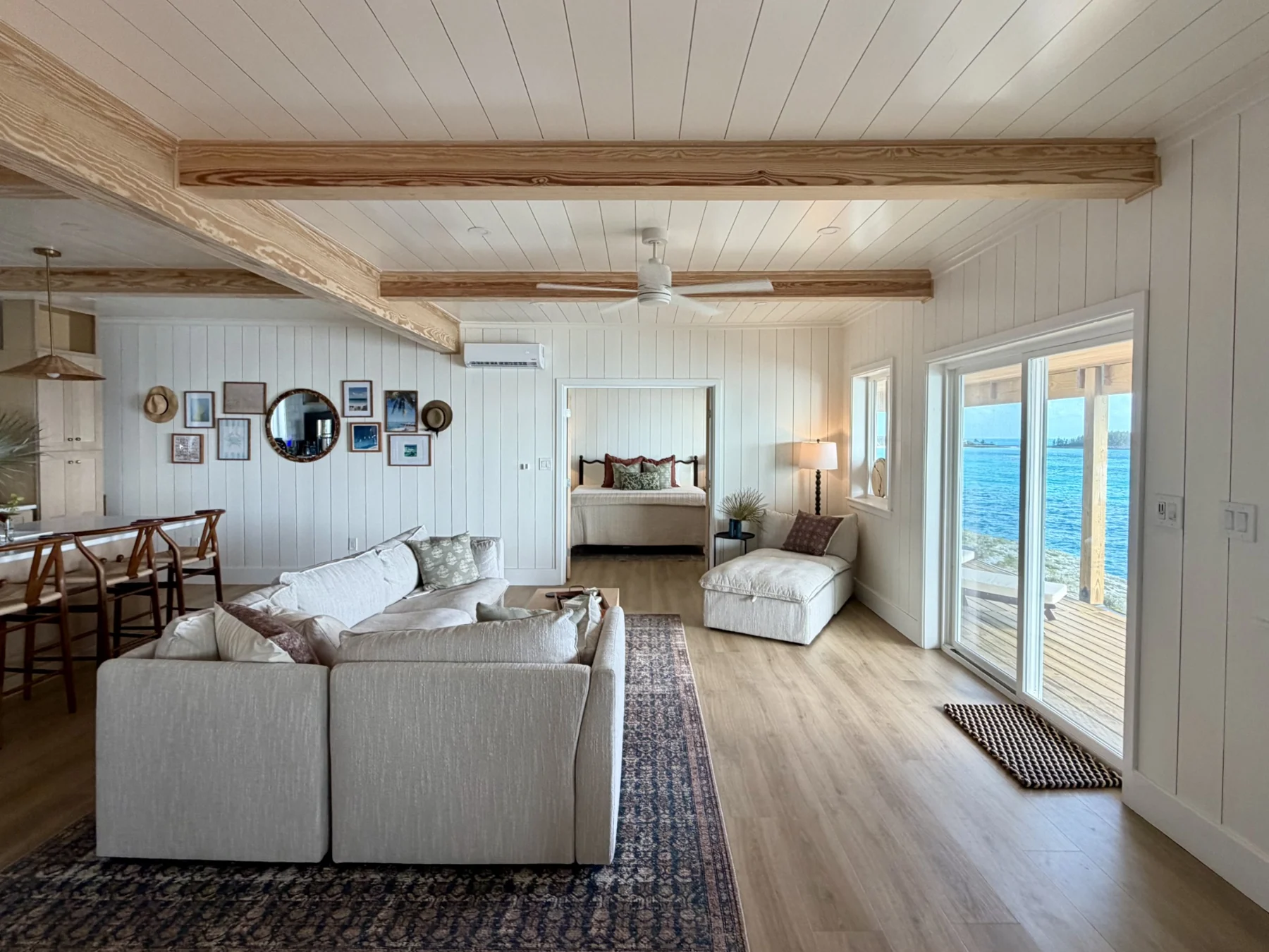 Pale sofas and timber ceiling beams in the CLIFFHOUSE living room, with glass doors facing the sea.