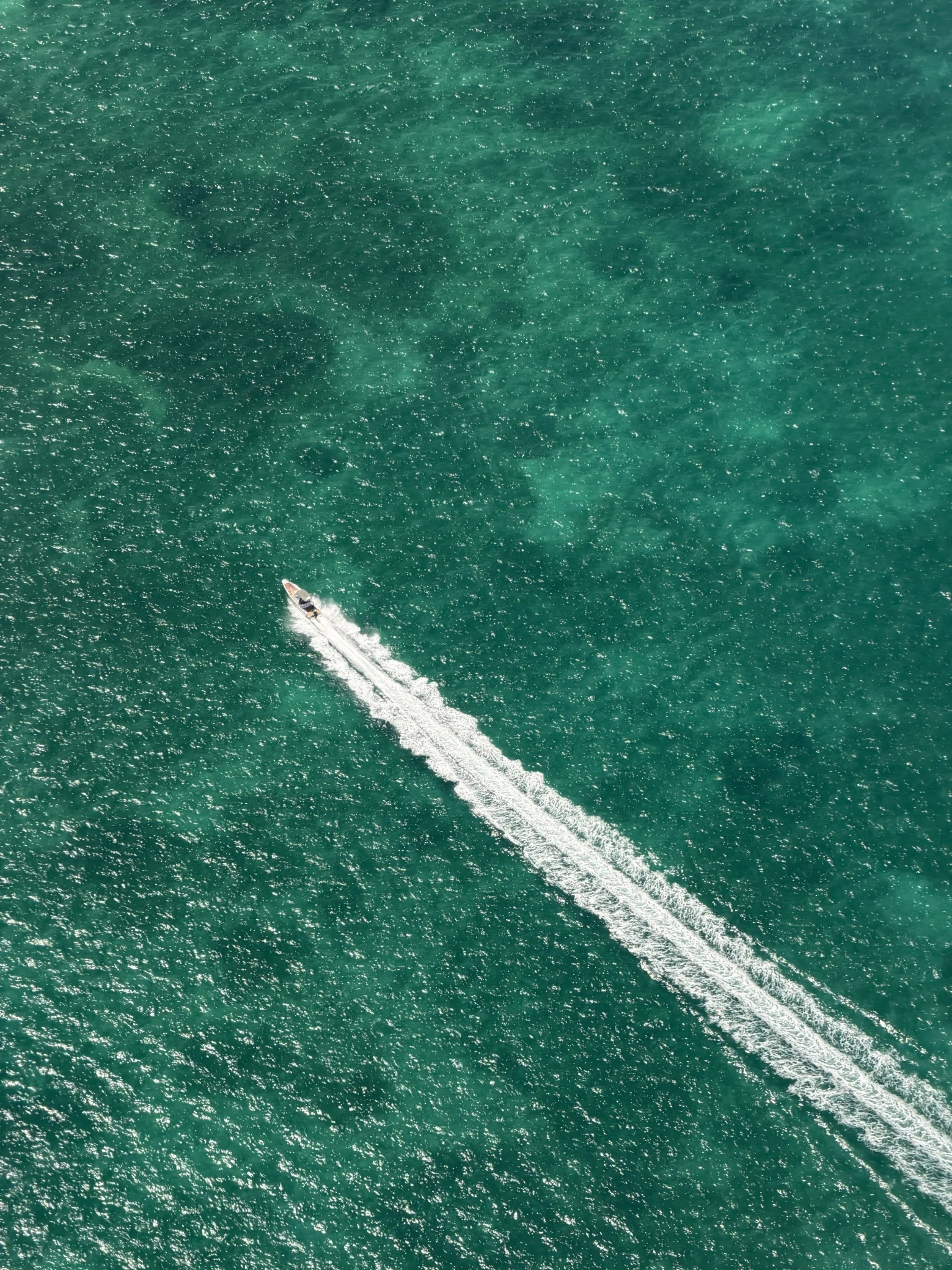 A small motorboat leaving a white wake across green-blue water, seen from above.